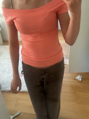 Korallfärgad offshoulder topp - Trendig korallfärgad offshoulder topp med tight passform. Toppen är ärmlös och har en bred kant upptill som ger en snygg axelbar look. Perfekt att styla med både jeans och kjol för en fräsch outfit.