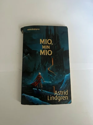 Mio, min Mio av Astrid Lindgren - En klassisk fantasybok av Astrid Lindgren med ett mystiskt och äventyrligt omslag i mörkblå toner. Boken handlar om Bo Vilhelm Olsson som blir Mio och ger sig ut på ett episkt äventyr i Landet i Fjärran. Perfekt för dig som gillar magi och spännande sagor.