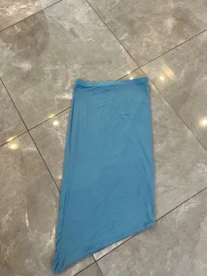Ljusblå asymmetrisk kjol från NA-KD - Trendig ljusblå kjol från NA-KD med asymmetrisk skärning. Kjolen har en enkel och stilren design i mjukt material som passar perfekt till sommaren. Midjemodell och utan synliga detaljer för en clean look. Kjolen är helt oanvänd 