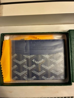 Blå korthållare  - Snygg blå korthållare med det klassiska vita och gråa mönstret. Tillverkad i läder och canvas, perfekt för kort och sedlar. Kommer i original grön box med gul putsduk. Stilren och lyxig accessoar för dig som gillar exklusiva detaljer.