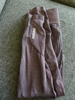 Lila seamless tights från Gymshark - Säljer ett par lila seamless tights från Gymshark med diskret randigt mönster och hög midja. Tightsen har logga på benet och är tillverkade i ett stretchigt funktionsmaterial som passar perfekt till träning och gym.