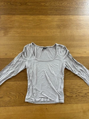 Beige långärmad topp Gina Tricot - Snygg beige långärmad topp från Gina Tricot med rundad, djup urringning. Tillverkad i mjukt och stretchigt material som sitter skönt på kroppen. Perfekt att styla med jeans eller kjol för en enkel och clean look.