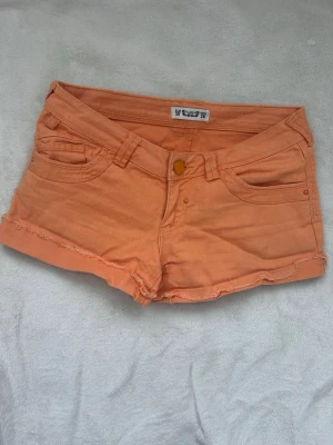 Orange denimshorts med fransig kant - Säljer ett par orangea denimshorts från Pull and bear med fransig kant nedtill. De har klassiska fem fickor, knappstängning och bälteshällor. Perfekta för varma dagar och ger en cool vibe till din outfit. Liten defekt på bild två, påverkar ej helhetsintrycket 😇