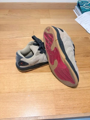  Jordan Flight sneakers - Snygga sneakers från Jordan i beige mocka med grå detaljer och svarta skosnören. Yttersulan är gummifärgad med röda partier undertill och den klassiska Jumpman-loggan syns på hälen. Perfekta för dig som gillar streetwear och vill sticka ut.