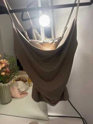 Beige linnetopp från Kappahl - Snygg beige linnetopp från Kappahl med tunna justerbara axelband och draperad urringning. Perfekt för dig som gillar en enkel men trendig look. Materialet känns mjukt och följsamt mot huden.