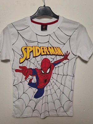 Vit Spiderman t-shirt Marvel - Cool vit t-shirt med stort Spiderman-tryck på framsidan och spindelnätsmönster. T-shirten har rund hals, korta ärmar och är gjord i mjuk bomull. Perfekt för dig som gillar superhjältar och vill sticka ut med en färgglad och ikonisk design.