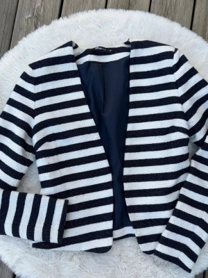 Randig kavaj från Gina Tricot (S) - Snygg kavaj från Gina Tricot i storlek 36. Kavajen har marinblåa horisontella ränder, öppen framtill och är fodrad. Materialet är stickat och ger en cool, avslappnad look. Perfekt för att lyfta vilken outfit som helst.