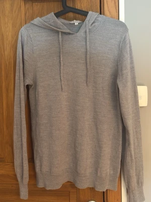 Ljusgrå hoodie med huva - En stilren ljusgrå hoodie med huva och dragsnören. Tillverkad i ett mjukt, tunt stickat material som känns skönt mot huden. Hoodien har långa ärmar och ribbade muddar vid ärmslut och nederkant. Perfekt för en avslappnad look.