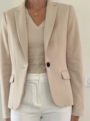 Beige kavaj stl 36 Ny - Klassisk beige kavaj med en knapp framtill. Kavajen har två fickor med lock fram och en klassisk krage. H&M stl 36. Ny.