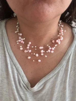 Halsband med söttvattenspärlor  - Unikt chokerhalsband med flera lager av tunna genomskinliga trådar dekorerade med oregelbundna rosa och vita pärlor. Halsbandet har en luftig och modern design som ger en romantisk känsla. Perfekt för dig som vill sticka ut med ett kreativt smycke.