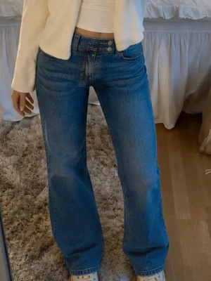 Blåa bootcut jeans med låg midja - Säljer ett par blåa bootcut jeans med låg midja och dubbla knappar i midjan. Jeansen har klassisk femficksdesign och är tillverkade i ett stretchigt denimtyg. Perfekta för en avslappnad och trendig look. S full length från lager 157