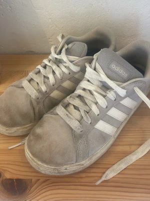 Grå Adidas Grand Court sneakers - Snygga grå Adidas Grand Court sneakers i mocka med vita ränder på sidorna och klassisk Adidas-logga på hälen. Skorna är smutsiga men kan tvättas och det kommer göras innan vi skickar iväg dem, annars i fint skick. Pris kan diskuteras💓