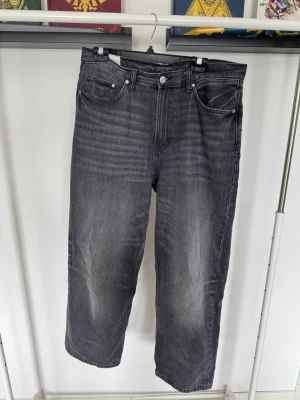 Grå raka jeans med tvättad look - Säljer ett par grå jeans med rak passform och tvättad look. Materialet är denim i bomull.