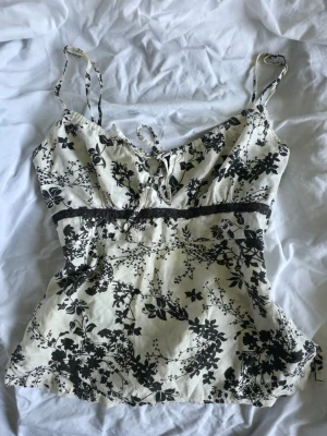 Blommig linnetopp från Lindex - Söt vintage topp från Lindex med svart blommigt mönster. Toppen har tunna axelband, knytning fram. 100 % Bomull. Storlek XS 💞