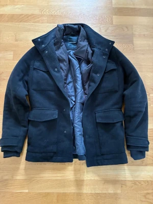 Svart rock från Jack & Jones Premium - Stilren svart rock från Jack & Jones Premium med klassisk krage och fyra stora fickor framtill. Rocken har quiltat innerfoder och stängs med både dragkedja och knappar. Perfekt för kalla dagar och snygg att matcha med jeans eller chinos.