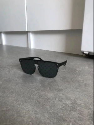 Svarta  solglasögon - Säljer ett par svarta solglasögon  med breda bågar och monogrammönster på glasen. Snygg, modern design med raka linjer och coola detaljer. Perfekta för dig som vill sticka ut och addera lyx till din stil.