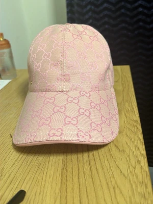 Rosa Gucci keps med monogram - Snygg rosa keps från Gucci med klassiskt GG-monogram i ljusrosa över hela kepsen. Justerbar rem bak i matchande färg och böjd skärm. Tillverkad i slitstarkt tyg som ger en exklusiv känsla och trendig look.