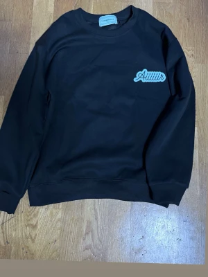 Svart sweatshirt Casablanca Aiit - Cool svart sweatshirt från Casablanca med tryck 'Aiit' på bröstet och stort färgglatt flygplansmotiv samt texten 'Casablanca Aiir' på ryggen. Tröjan har rund halsringning och ribbade muddar. Perfekt för dig som gillar streetwear och grafiska prints. OBS LITEN I STLRK PASSAR SOM XS 