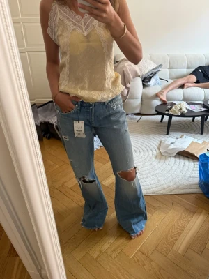 Bootcut jeans zara - slutsålda konstant!! Säljer ett par ljusblå bootcut jeans från Zara med slitningar och stora hål vid knäna. Jeansen har klassisk femficksmodell och är tillverkade i denim. Perfekta för en avslappnad och trendig look.