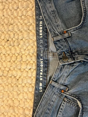 Blå low straight jeans waist 32/34 - Säljer ett par klassiska blå jeans med low straight passform och waist 32, length 34. Jeansen har fem fickor, metallknappar och är gjorda i slitstark denim. Perfekta för dig som gillar en avslappnad och tidlös look.