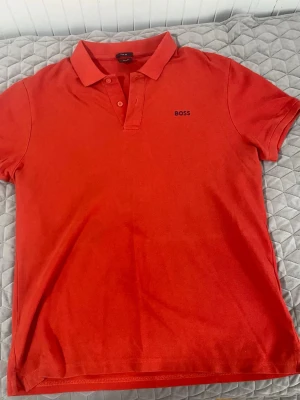 Röd slim fit t-shirt från BOSS - Snygg röd t-shirt från BOSS i slim fit-modell. Klassisk pikékrage med knappar och diskret BOSS-logga på bröstet. Perfekt för dig som gillar stilrena och enkla plagg med en modern passform.