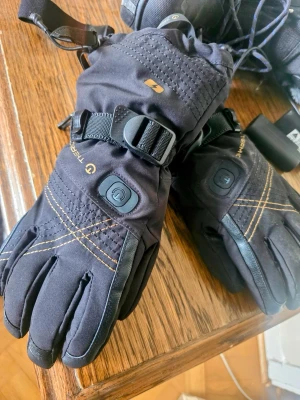 Svarta Thermic värmehandskar syl 7  - Säljer ett par svarta värmehandskar från Thermic med justerbart spänne och synliga sömmar i kontrastfärg. Handskarna har inbyggd värmefunktion och är perfekta för kalla dagar. Snygg och funktionell design med detaljer i svart och gult. Använd 2 gånger så i absolut nyskick 