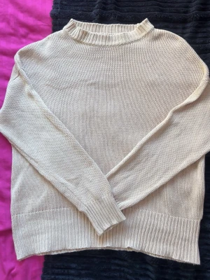 Beige stickad tröja med ribbade detaljer - En enkel och beige stickad tröja med rund hals och ribbade muddar vid ärmslut och nederkant. Tröjan har en avslappnad passform och är perfekt för lager på lager. Materialet känns mjukt och bekvämt mot huden.