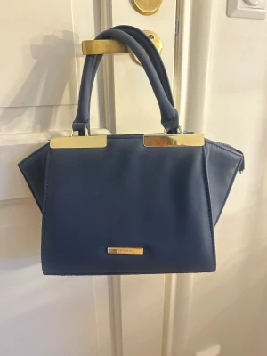 Mörkblå handväska från Calvin Klein - Mökblå handväska med guldfärgade metalldetaljer