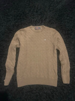 Brun kabelstickad tröja Morris - Säljer en brun kabelstickad tröja från Morris i 100% merinoull. Tröjan har rund halsringning, ribbade muddar och en liten broderad logga på bröstet. Perfekt för dig som gillar klassisk och stilren design. Storlek M men sitter mer som S.