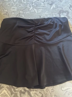Svart kjol med rynkad midja - Stilren svart mini kjol med hög midja och snygg rynkdetalj framtill. Kjolen har en lätt utsvängd form och materialet är mjukt och följsamt, perfekt för en trendig look. Passar till många olika stilar och är enkel att matcha. Endast använt en gång !!!!