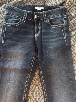 Mörkblå jeans med broderade fickor - Snygga mörkblå lågmidjade jeans ifrån Gina Tricot. Modellen är Bootcut och i storlek 158. Passar nån som är upp till 165 och byxan motsvarar XXS/XS. Jätte snygga fickor och knappt använda (1-2 gånger bara)  