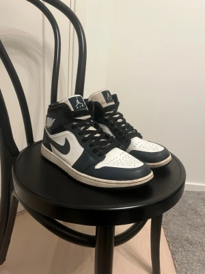 Air Jordan 1 Mid armory Navy - Snygga Air Jordan 1 Mid sneakers i marinblått och vitt läder med svarta detaljer.