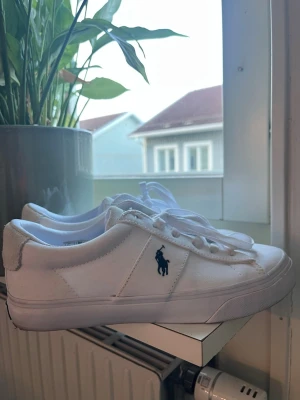 Vita sneakers från Polo Ralph Lauren - Snygga vita sneakers från Polo Ralph Lauren med klassisk låg profil och marinblå logga på sidan. Säljer dom pågrund av för stor storlek, och är använd 2 gånger. Köpte skorna för 1300 kr. Priset kan eventuellt diskuteras.