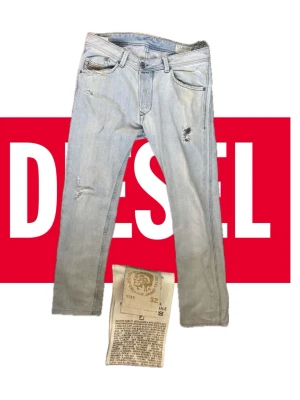 Ljusblå slitna jeans från Diesel - Säljer ett par ljusblå jeans från Diesel med snygga slitningar och raka ben. Jeansen har klassisk femficksmodell och är tillverkade i bomull. Perfekta för en avslappnad och trendig look.