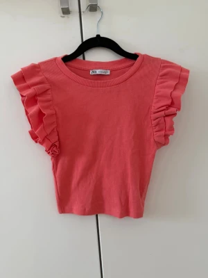 Korall ribbad topp med volangärmar Zara - Supersöt Korral topp från Zara med ribbad struktur och volangdetaljer på ärmarna. Modellen är croppad och har rund halsringning. Perfekt för dig som vill ha en färgglad och trendig topp till sommaren. En väldigt trendig färg som passar väldigt bra nu till sommar då man blir brun.