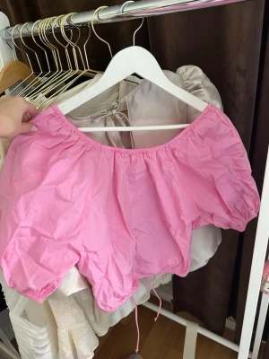 Rosa offshoulder croppad topp - Söt rosa offshoulder topp med puffiga korta ärmar och croppad passform. Toppen har snörning i ryggen som ger en extra detalj. Perfekt för sommarens alla tillfällen.