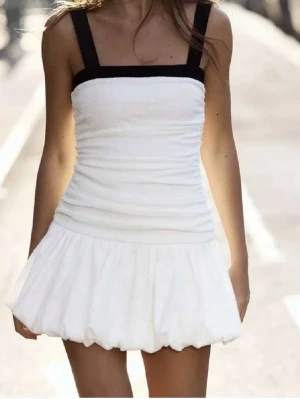 Vit kort klänning från Zara - Supersöt vit kort klänning från Zara med svarta axelband. Kjolen har en ballongformad volangkant nertill. Dragkedja i midjan. 