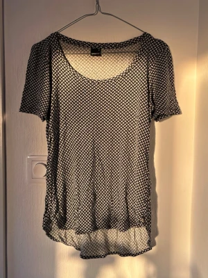 Svartvit mönstrad t-shirt - Snygg svartvit t-shirt med rund halsringning och korta ärmar. T-shirten har ett tätt, grafiskt mönster och är något längre baktill för en avslappnad look. Perfekt till jeans eller shorts.