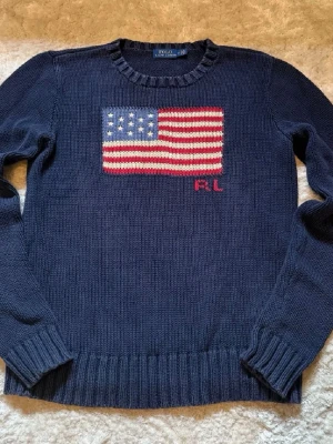 Mörkblå stickad tröja Polo Ralph Lauren - Säljer en klassisk Polo Ralph Lauren stickad tröja med den ikoniska amerikanska flaggan på bröstet. En riktig Ralph Lauren-ikon som aldrig går ur tiden.  ✅ Märke: Polo Ralph Lauren ✅ Färg: Marinblå ✅ Mått: [skriv privat] ✅ Storlek: [Barn M men passar XS/S] ✅ RL-brodyr under flaggan ✅ Bekväm och tidlös modell – passar året runt  Tröjan är i fint begagnat skick, mjuk och skön med exklusiv känsla. 📌 Nypris ligger oftast runt 3000.
