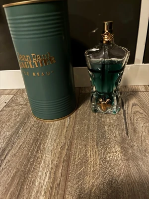 Jean Paul Gaultier Le Beau parfym - Jean Paul Gaultier Le Beau parfym i en unik flaska formad som en manlig torso med blågrön vätska och gulddetaljer. Kommer med original grön metalltub med guldfärgad text. Flaskan har en exklusiv och konstnärlig design. Mycket kvar