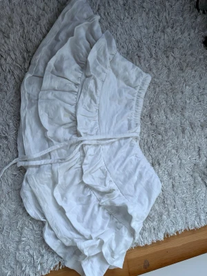 Vit volangkjol från Gina Tricot - Supersöt vit kortkjol från Gina Tricot med volangdetaljer och omlottknytning i midjan. Kjolen har en luftig känsla och passar perfekt till varma dagar. Elastisk midja för skön passform och trendig look. Storlek S. Pris kan diskuteras 💕