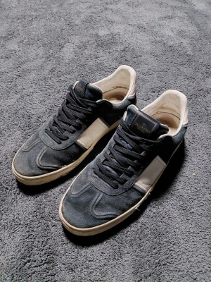 Mörkblå Valentino Flycrew - Ett par sällsynta valentino flycrews i färgen mörkblå size 44. De är i okej skick men har tappat ett par nitar och sömmen har låssnat på vissa delar av sulan(fråga efter bild om du undrar). Mockan är bra men lädret har en liten "spricka" på den vita "stripen". Skriv om du har fler frågor😁