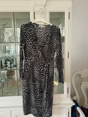 Leopardmönstrad omlottklänning Michael Kors - Säljer en snygg leopardmönstrad omlottklänning från Michael Kors. Klänningen har lång ärm, v-ringning och knyt i midjan. Färgerna går i svart och grått, och materialet känns mjukt och stretchigt. Perfekt för dig som vill sticka ut med ett djurmönster.