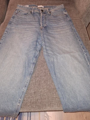Ljusblå raka jeans från Nudie - Säljer ett par klassiska ljusblå jeans från Nudie med rak passform och fem fickor. Jeansen har en vintage tvätt och Nudie-loggan på bakfickan. Tillverkade i 100% bomull för en skön och avslappnad känsla.