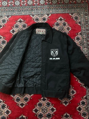 Doge Ram Jacka - Dodge Ram / RAM Trucks Workwear Jacket.  Really cool jacket with a small logo on the front and a large one on the back.  Gently used, in great condition.  Lighty padded on the inside, perfect for spring and summer.  Has adjustable waist with button tabs, check 2nd picture, for a customizable fit.  Two front pockets, one interior pocket and a small pocket on left sleeve.  Size XL.  Lenght 69cm Width 66cm  If you have any questions or offer, let me know:)  