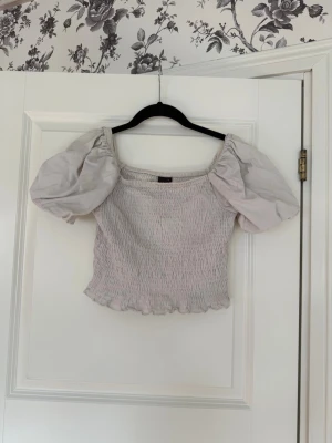 vit topp med puffärmar  - Supersöt vit topp med puffiga kortärmar och smockad kropp. Toppen har en croppad passform och volangkant nedtill, storlek s från gina Tricot.