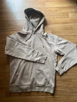 Beige jack & Jones  hoodie - Snygg beige hoodie med klassisk känguruficka och justerbar huva med dragsko. Hoodien har ribbade muddar vid ärmslut och nederkant. Perfekt för en avslappnad och stilren look. Materialet känns mjukt och bekvämt mot huden.