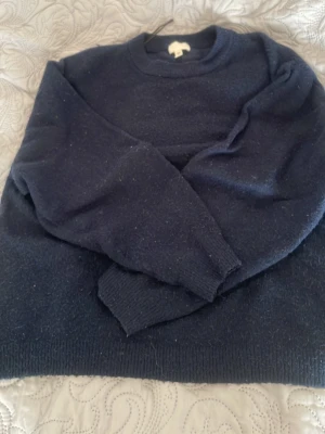 Mörkblå stickad tröja från H&M - Mysig mörkblå stickad tröja från H&M med rund halsringning och ribbade muddar vid ärmslut och nederkant. Perfekt för kyliga dagar och enkel att matcha med olika outfits. Klassisk modell som passar till det mesta. Något nopprig