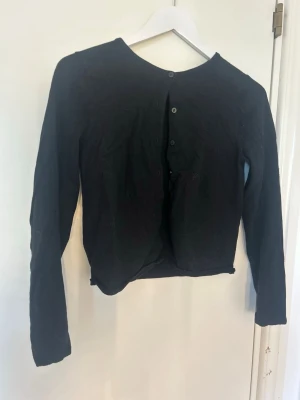 Svart kofta från H&M - En enkel svart kofta från H&M med rund halsringning och knäppning framtill. Koftan har långa ärmar och är tillverkad i ett mjukt material som passar perfekt till lager på lager. Stilren och lätt att matcha med olika outfits.