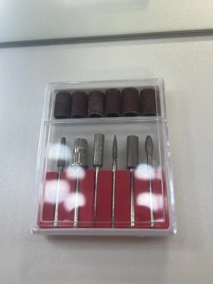 Nagelfil-borrset i metall och sand - Ett set med sex olika nagelborrar i metall och sex bruna sliprullar i sandpapper, perfekt för elfil till naglar. Kommer i en genomskinlig plastask med röd insida. Passar för både manikyr och pedikyr när du vill fixa naglarna hemma.